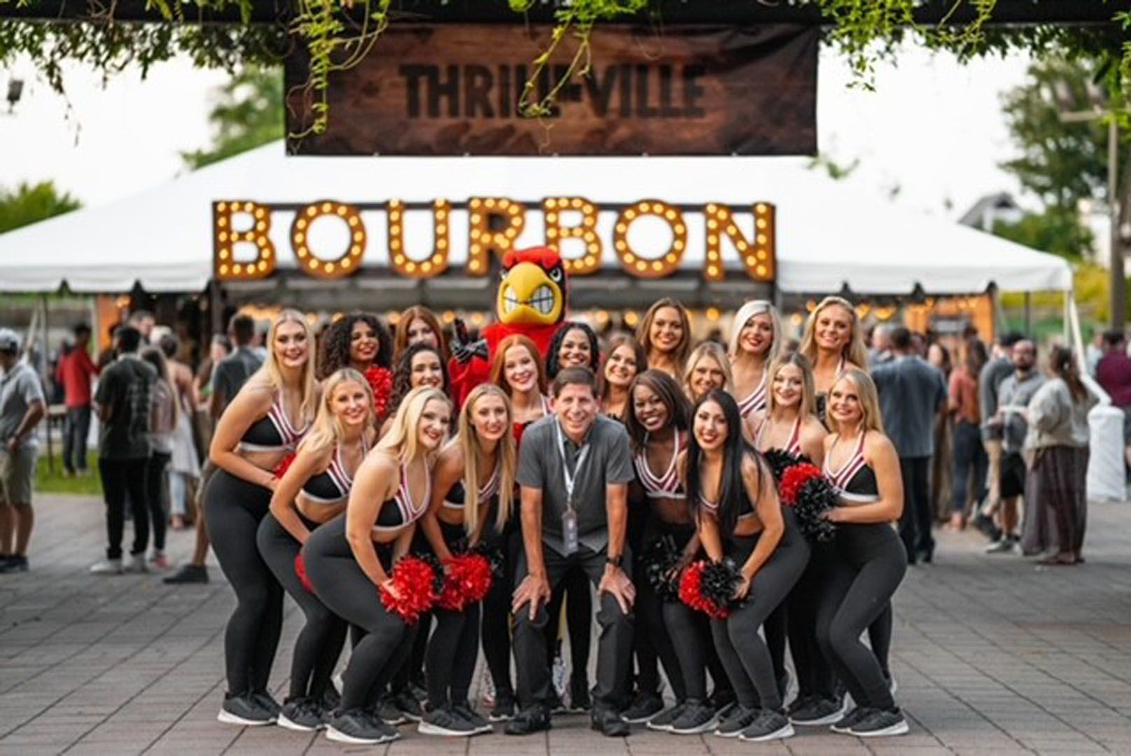 A group of cheerleaders are posing for a picture in front of a bourbon sign.