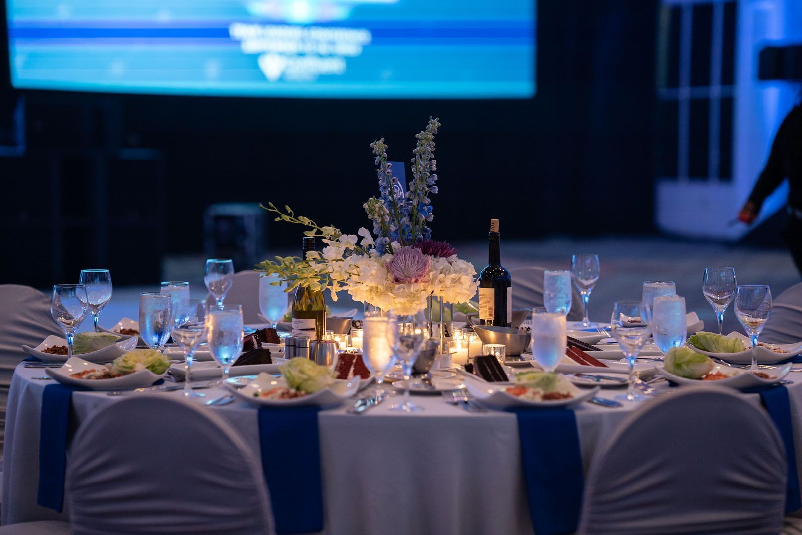 A table set for a wedding reception with a large screen in the background