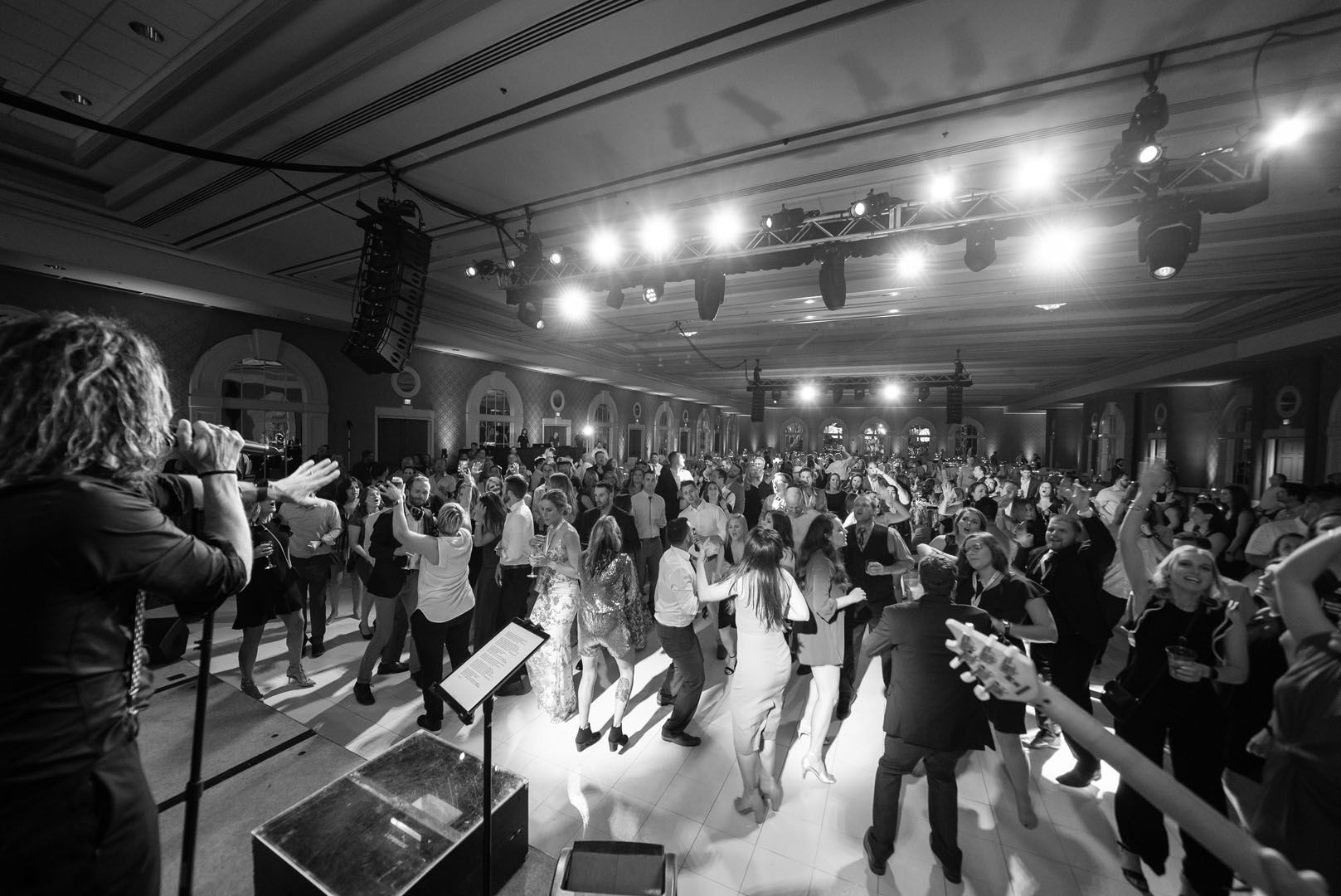A black and white photo of a group of people dancing in a large room.