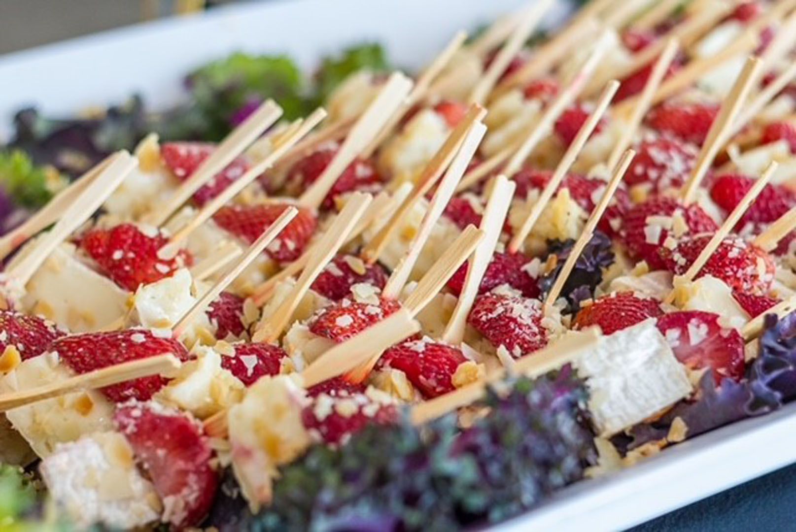 A close up of a plate of food with strawberries and cheese on skewers.