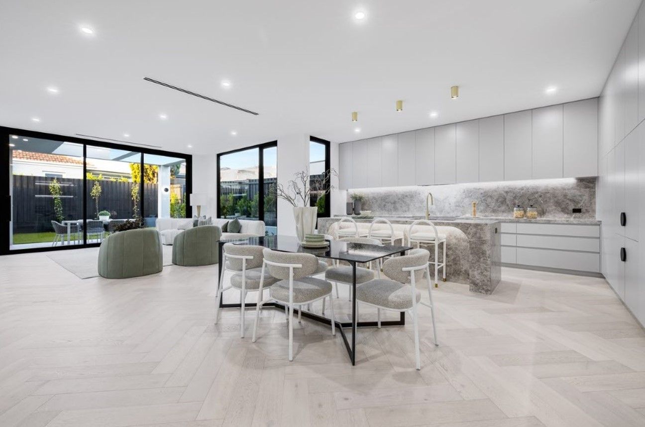Modern open-plan kitchen and living area with marble island, light wood flooring, and large windows.