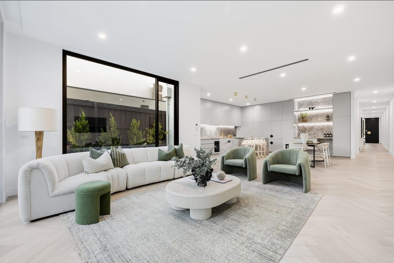 Modern living room with white walls, large window, light-colored sofa, green armchairs, and a rug.