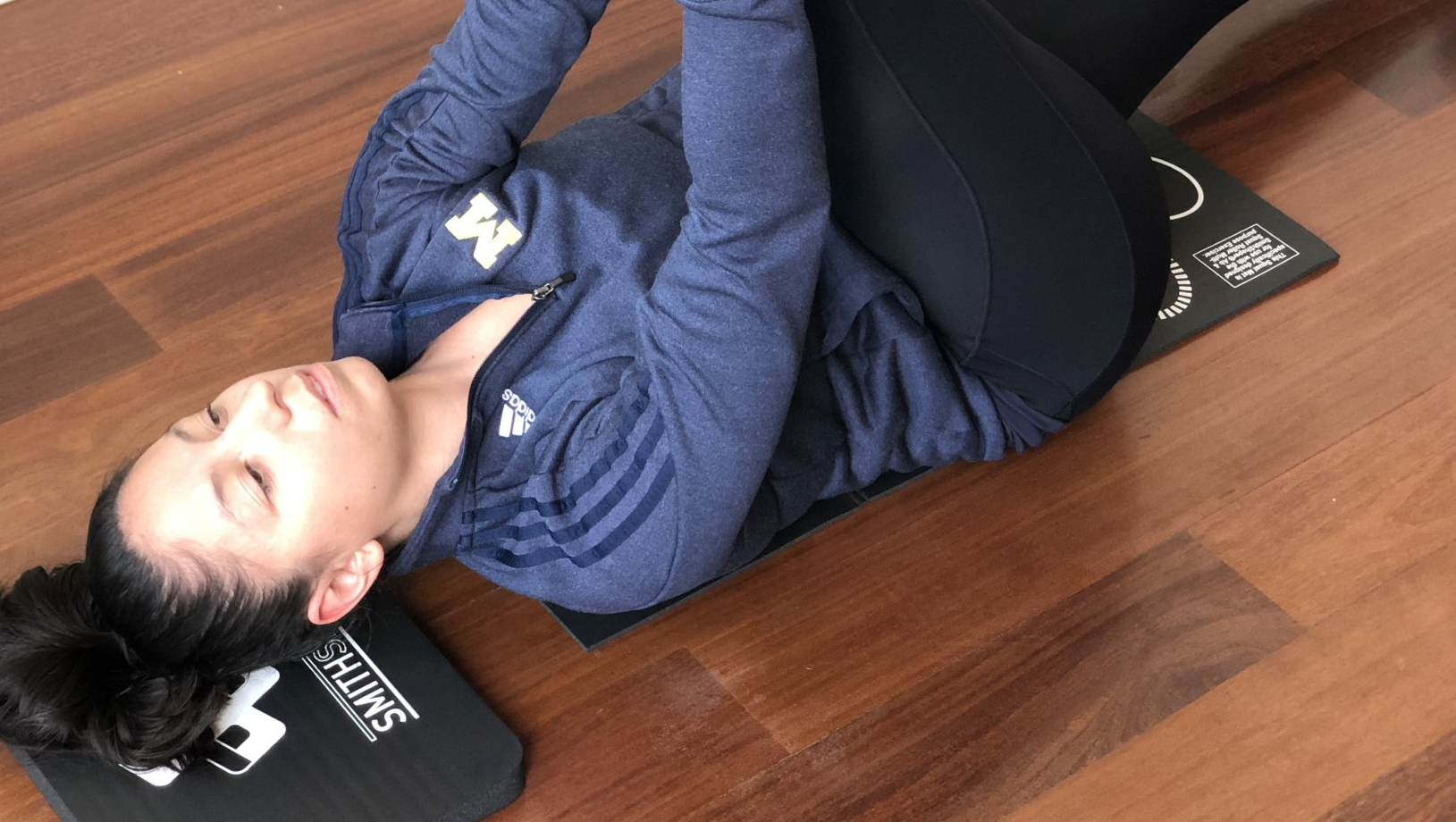 A woman stretches as she rests her head on a SmithShaper Super Pad and her back on an unfolded SmithShaper Squat Mat