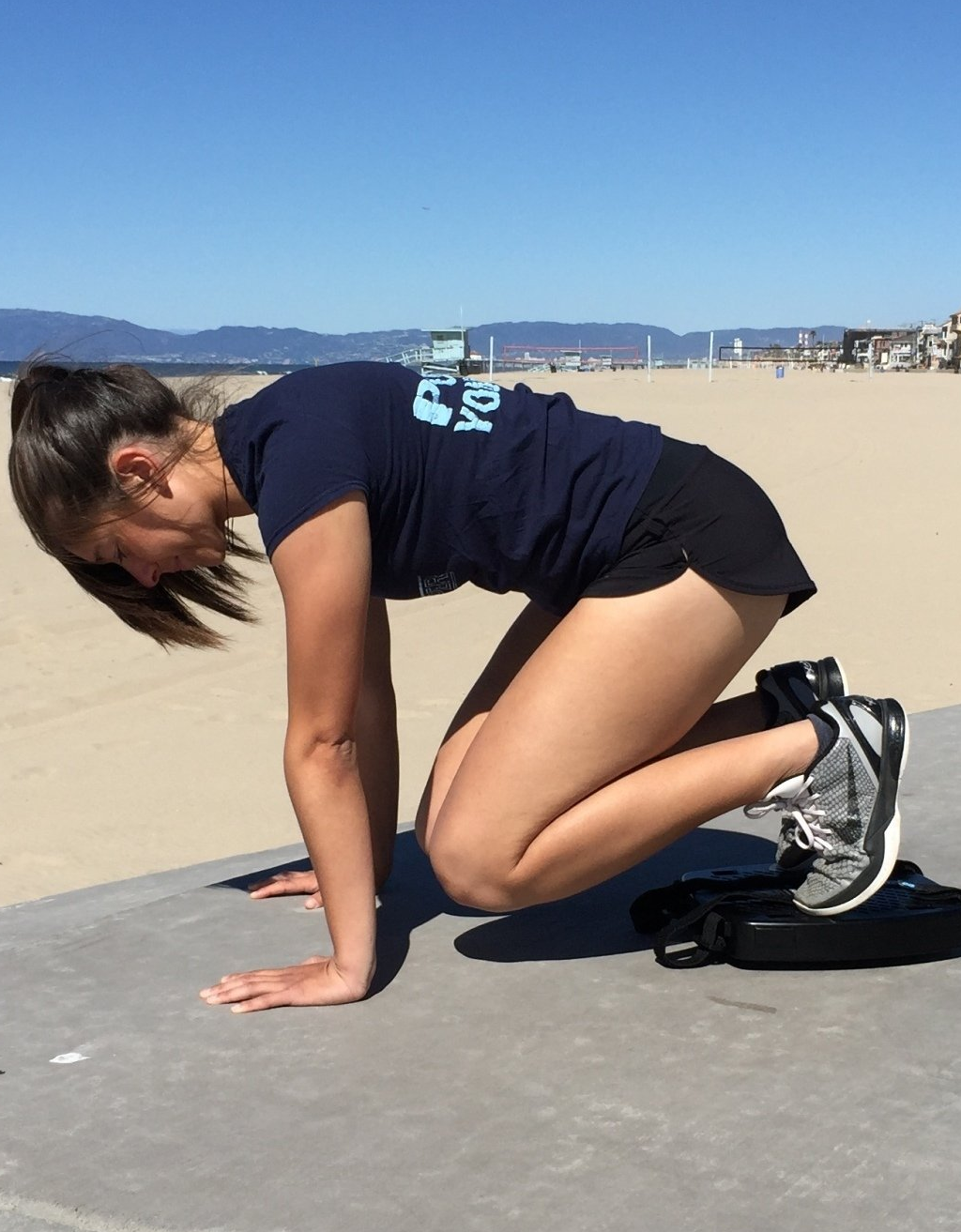 A woman on a beach sidewalk is using a SmithShaper ASR to perform the SmithShaper Core Crusher exercise
