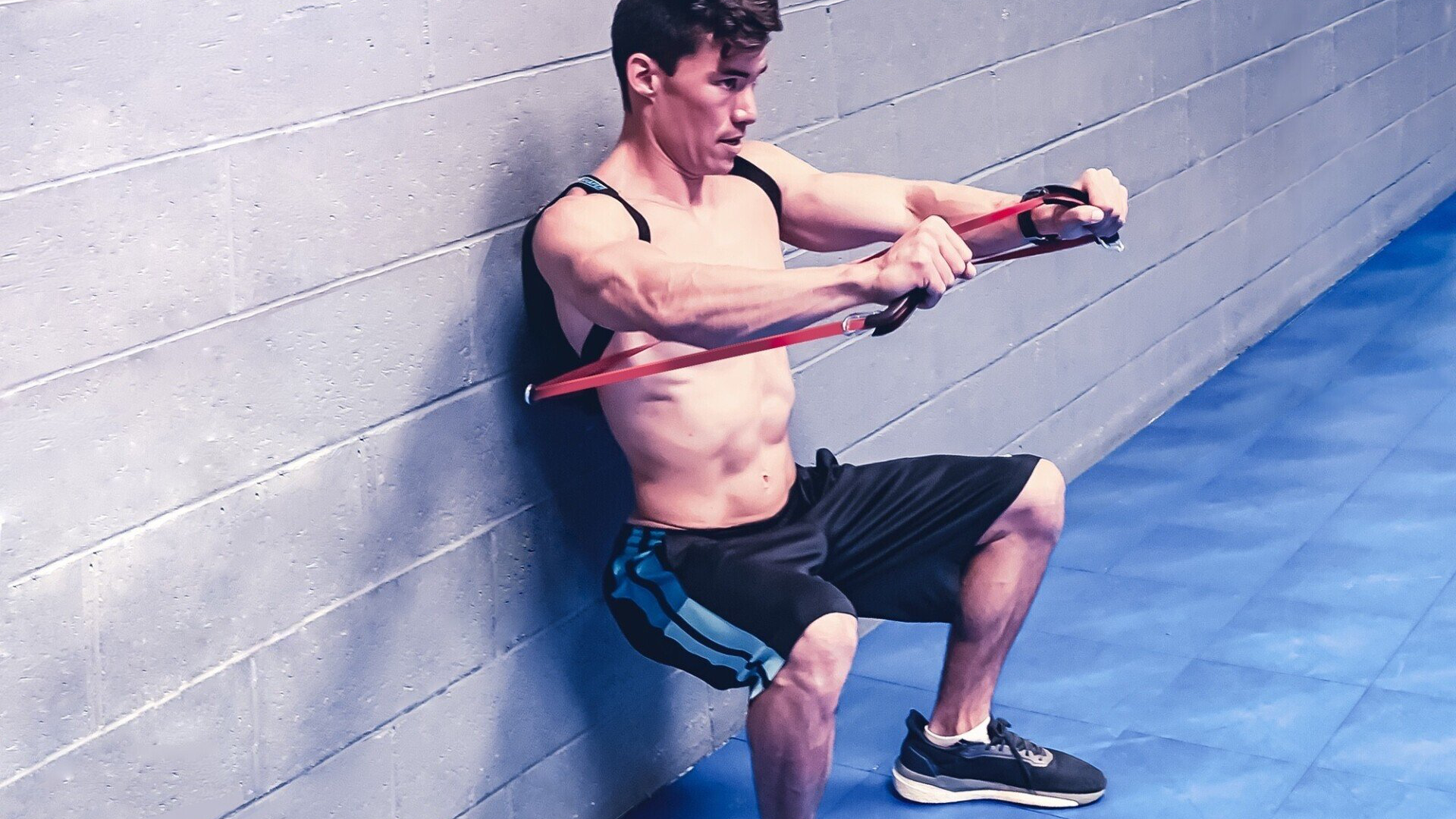 Shows a man wearing the SmithShaper SQUATX multipurpose combination exerciser where he performs rolling wall squats while simultaneously doing resistance band chest presses with SmithShaper high-stretch loop resistance bands anchored on the SQUATX device.