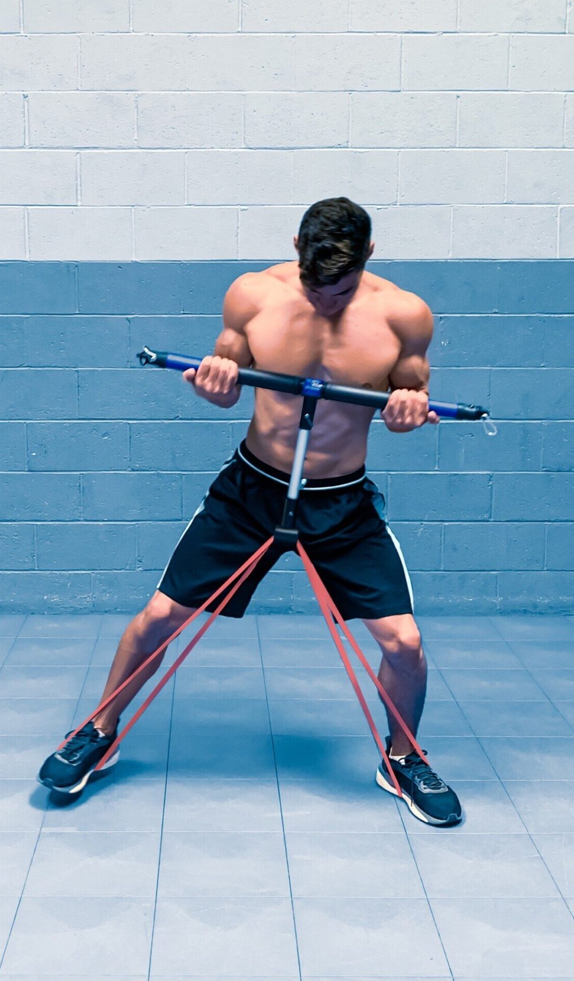 a shirtless man in black shorts is shuffling as he performs SmithShaper Biceps Curl and Leg Jacks or Shuffle resistance band exercise using a TR-BAR PLUS exerciser connected to a red SmithShaper 42-inch Zobo Sports High Stretch Therapy Resistance Loop Band anchored on each of her feet