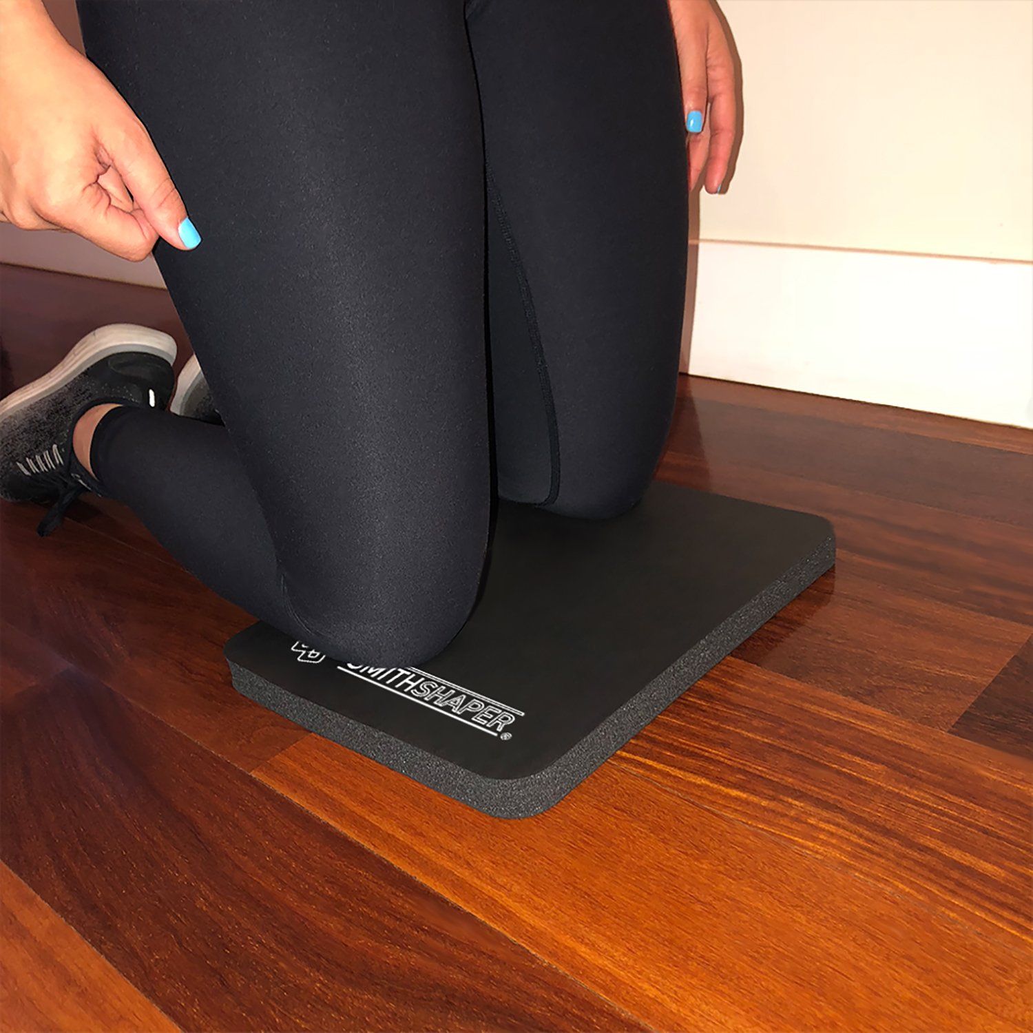 shows a woman in black leggings cushioning her knees on a black SmithShaper Super Pad thick exercise kneeling mat