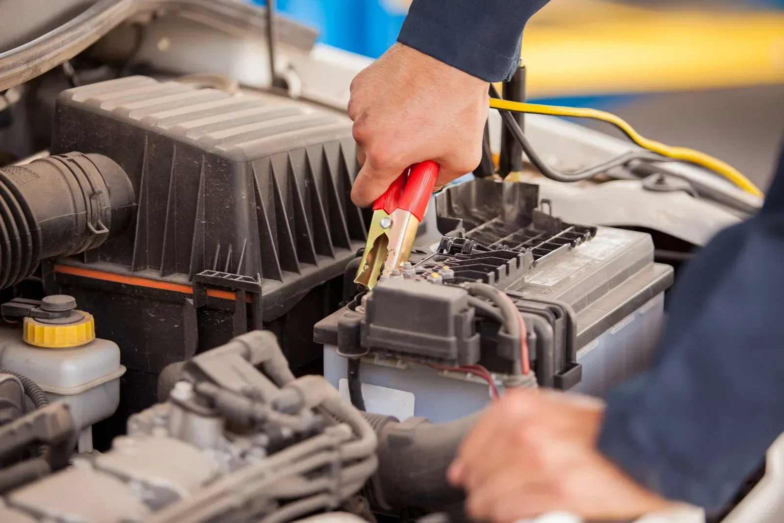 Hands connecting jumper cables to a car battery in an engine bay.