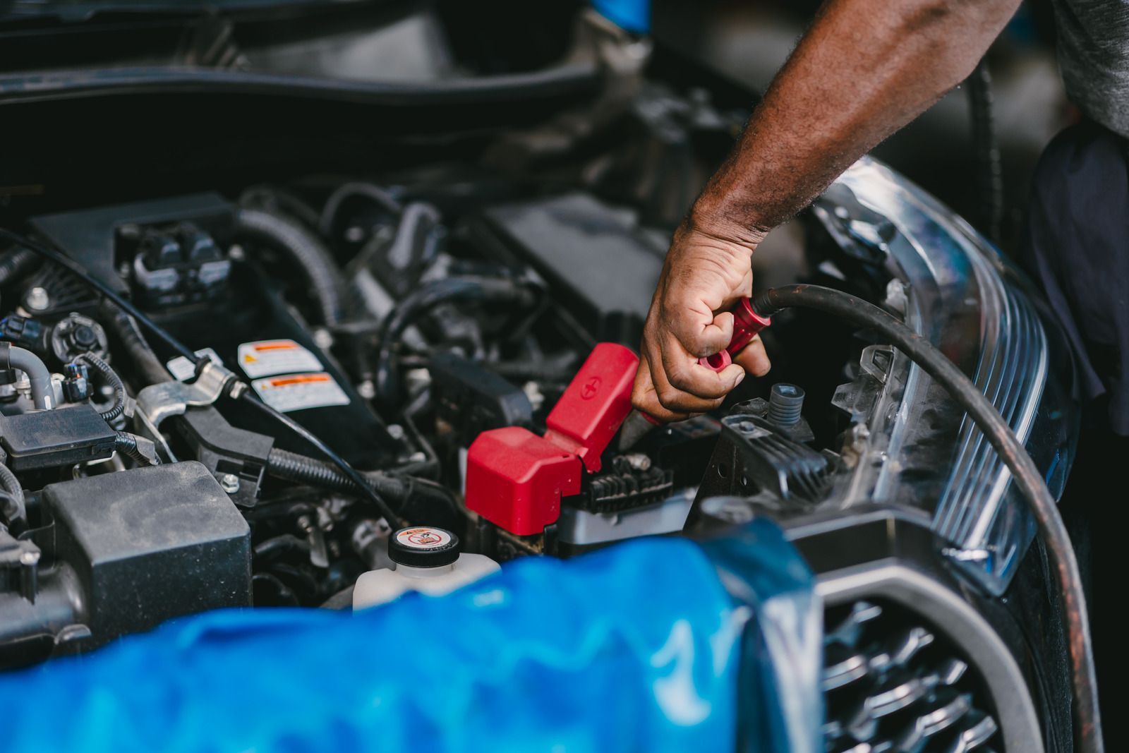 Person working on car engine, connecting cables to the battery.
