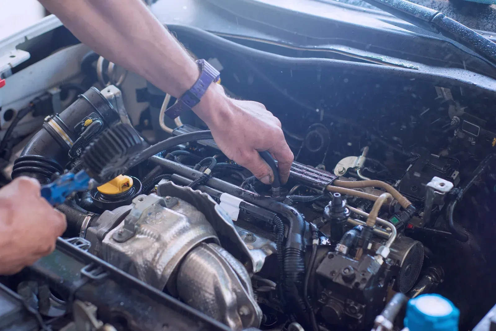 Person washing a car engine with water, outdoor setting.