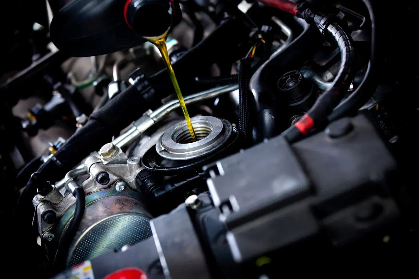 Pouring oil into a car engine; yellow oil, dark engine components, black tubes and wires.