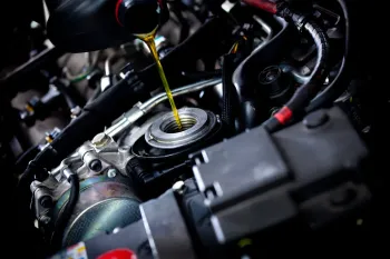 Pouring oil into a car engine; yellow oil, dark engine components, black tubes and wires.