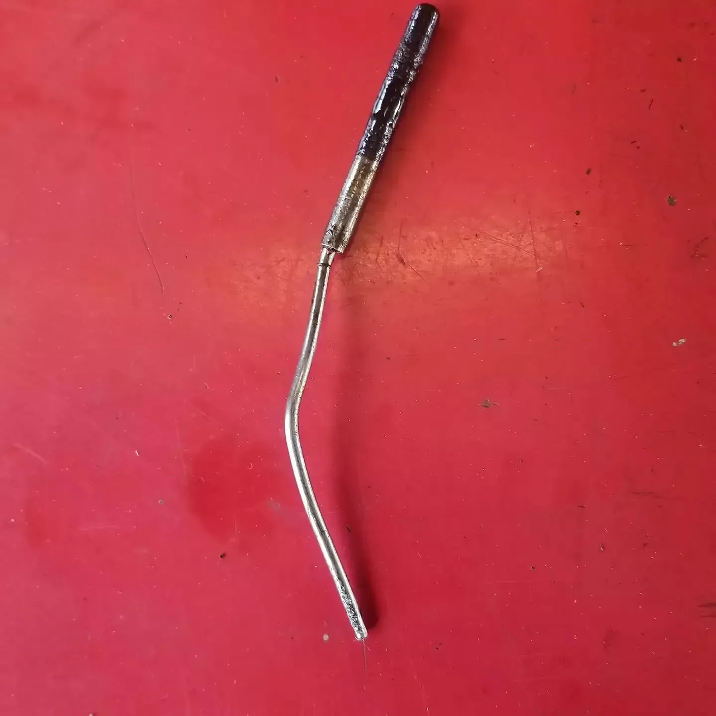 Bent, silver metal rod with a black handle on a red surface.