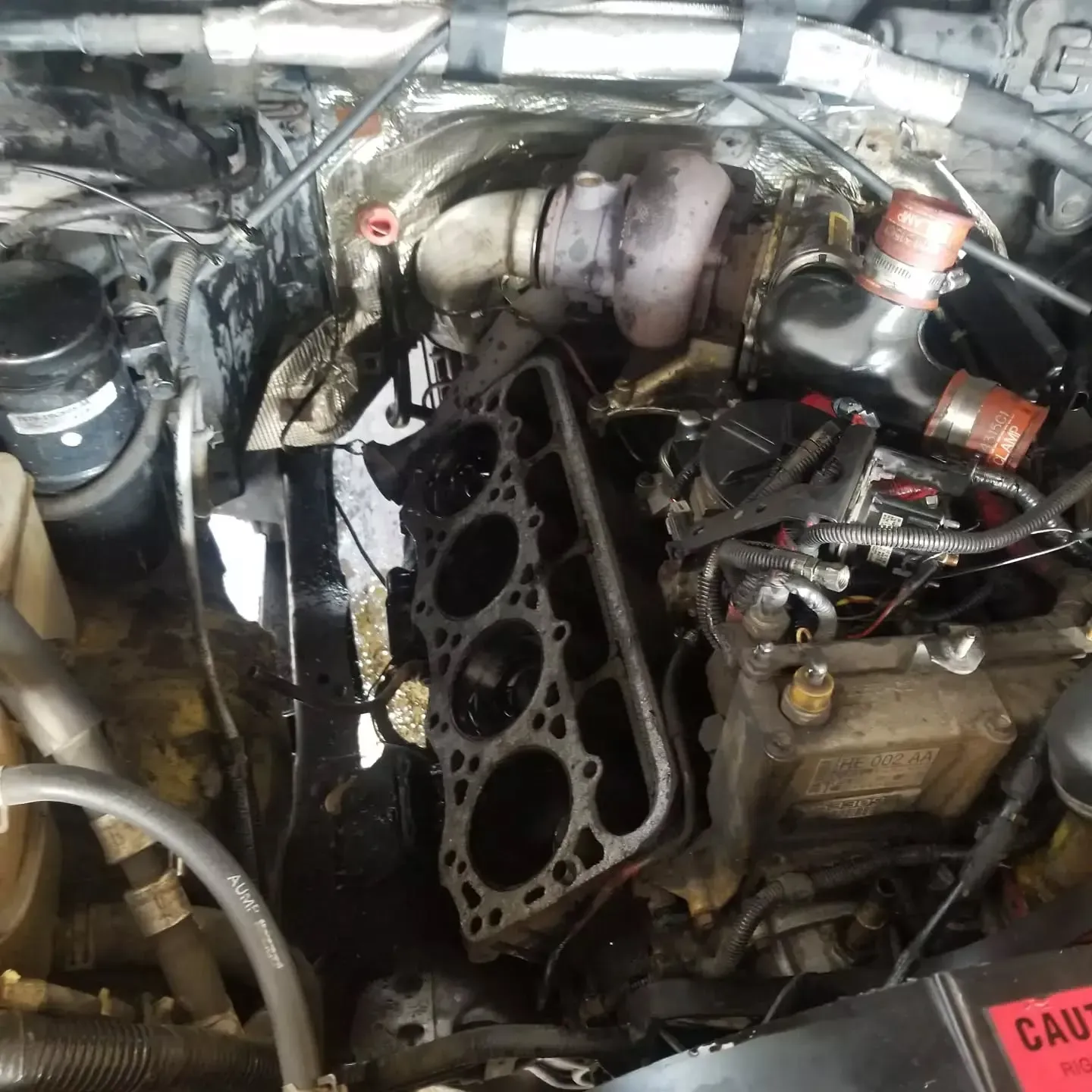 Engine components of a truck, including a cylinder head and turbocharger, are visible during repair.