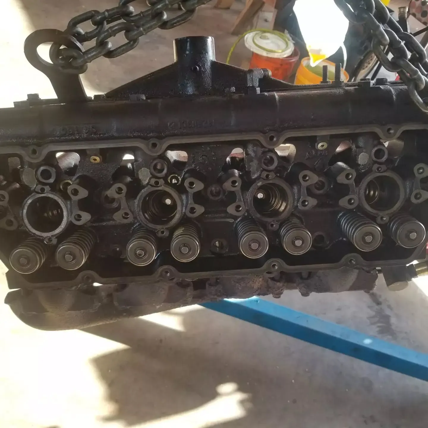 Black engine block being lifted by a chain, outdoors.