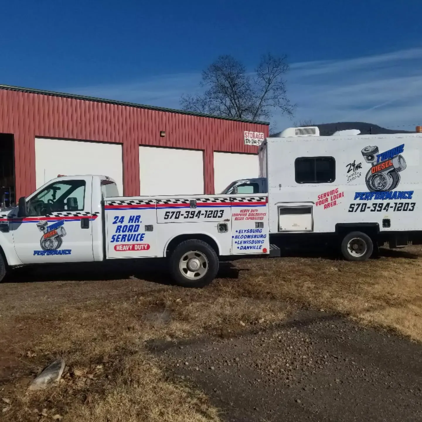 A white tow truck and trailer with Performance logos parked in front of a red building on a sunny day.