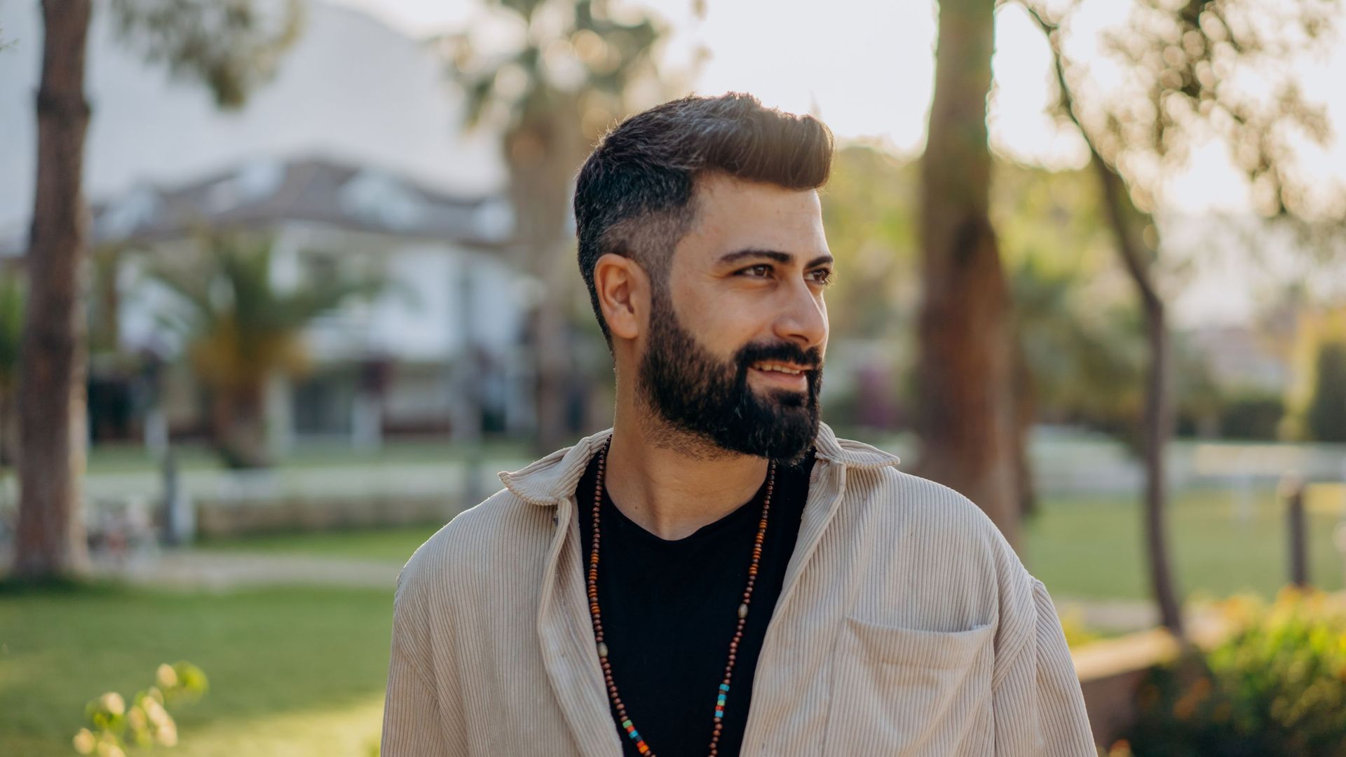 A man with a beard is standing in a park.