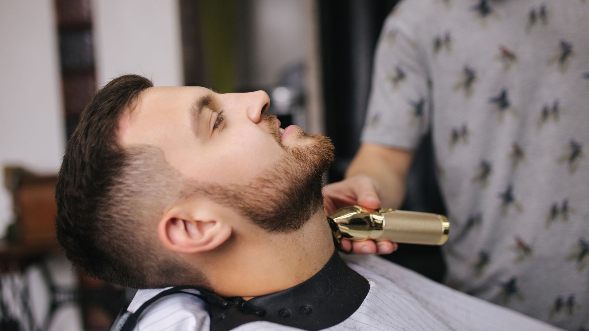 A man is getting his beard trimmed by a barber in a barber shop.