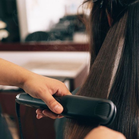 A woman is getting her hair straightened by a hairdresser.