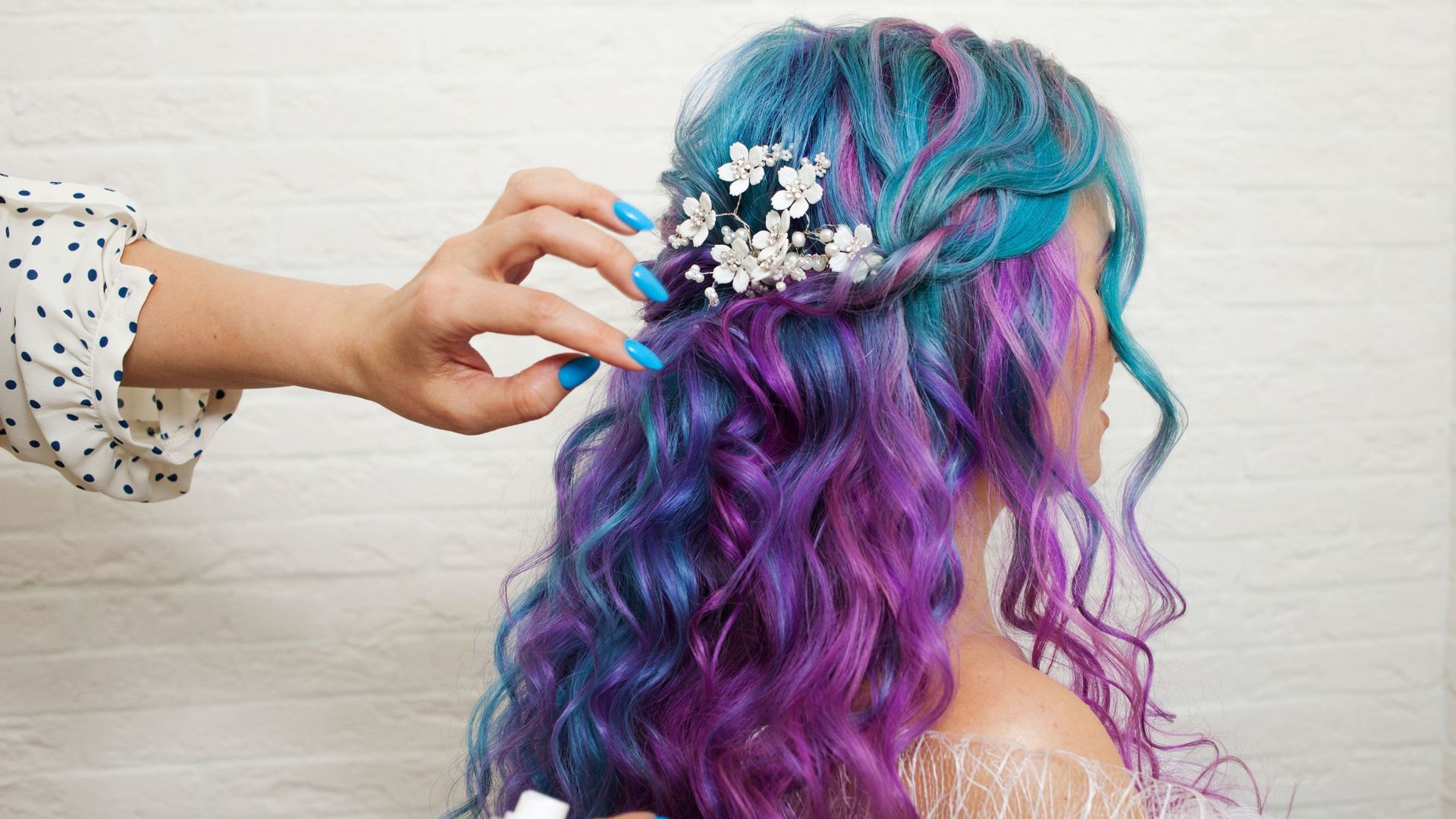 A woman with blue and purple hair is getting her hair done by a hairdresser.
