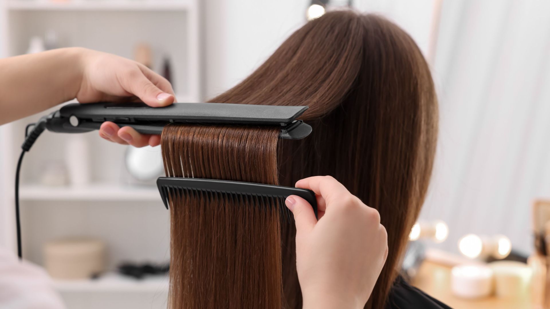 A woman is getting her hair straightened by a hairdresser.