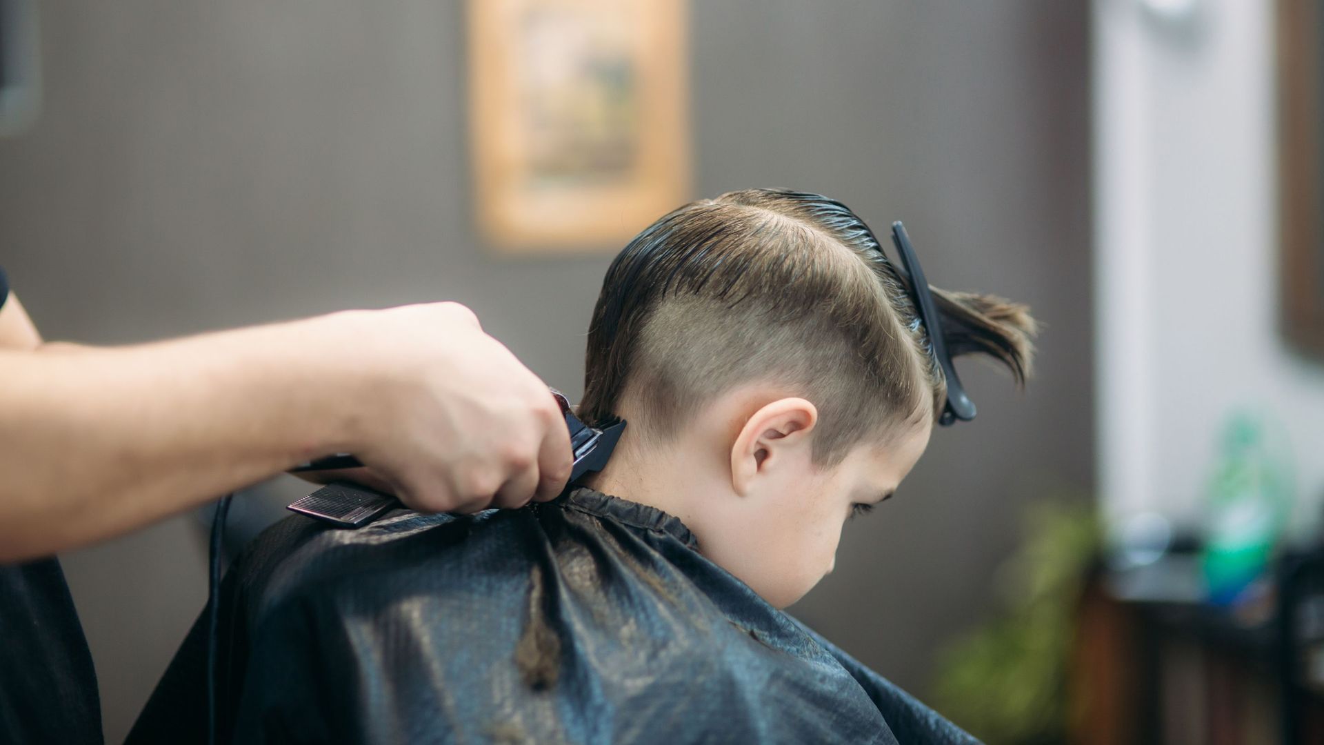 A young boy is getting his hair cut by a barber in a barber shop.