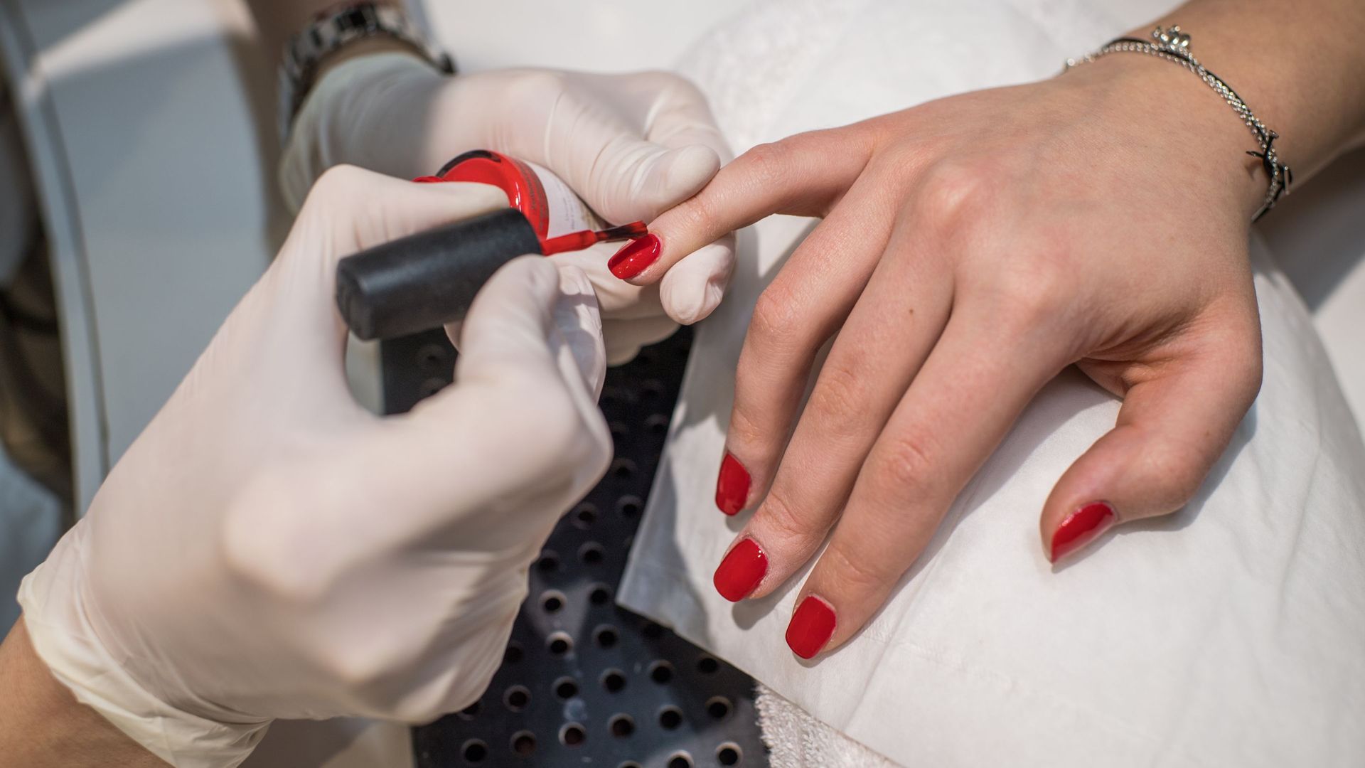 A woman is getting her nails painted red by a nail artist.