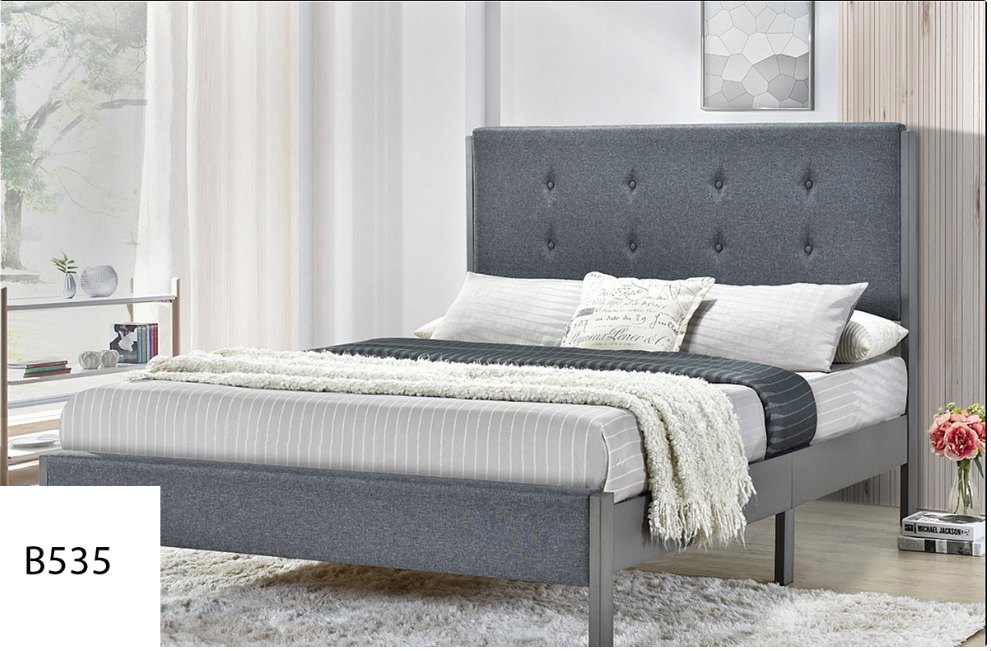 A bed with a grey headboard and white sheets in a bedroom.