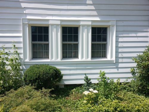 A white house with three windows and bushes in front of it