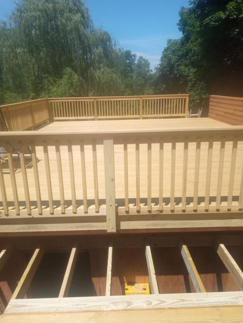 A wooden deck with a railing and trees in the background.