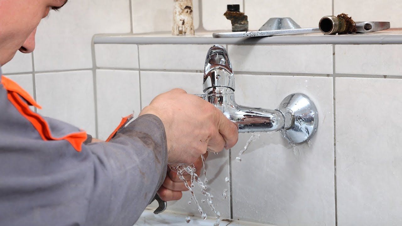 Plumber fixing a leaky tap in Kingston kitchen using spanner