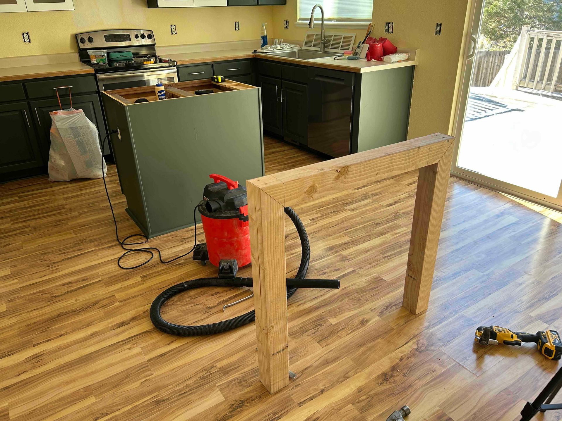Kitchen under construction; wood frame on floor, cabinets, appliances, and island.
