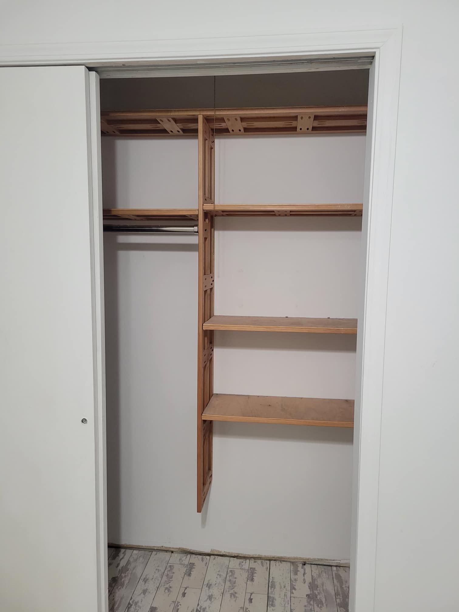 Closet with wooden shelves and a rod, built into a white wall, with a sliding door on the left.