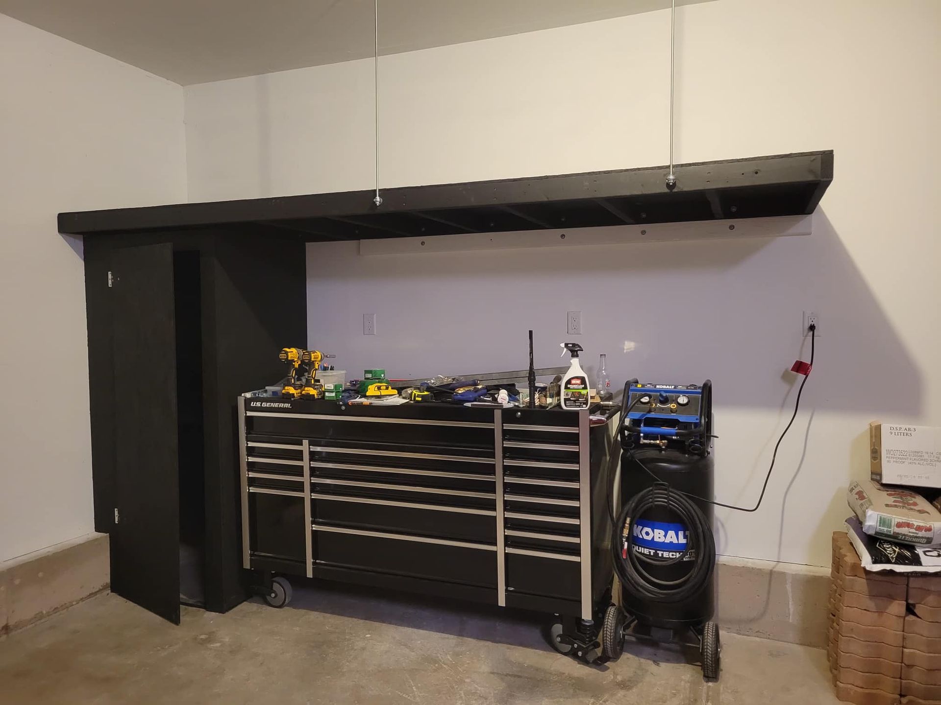 Black toolbox, cabinet, and shelf against a white garage wall, tools on top.