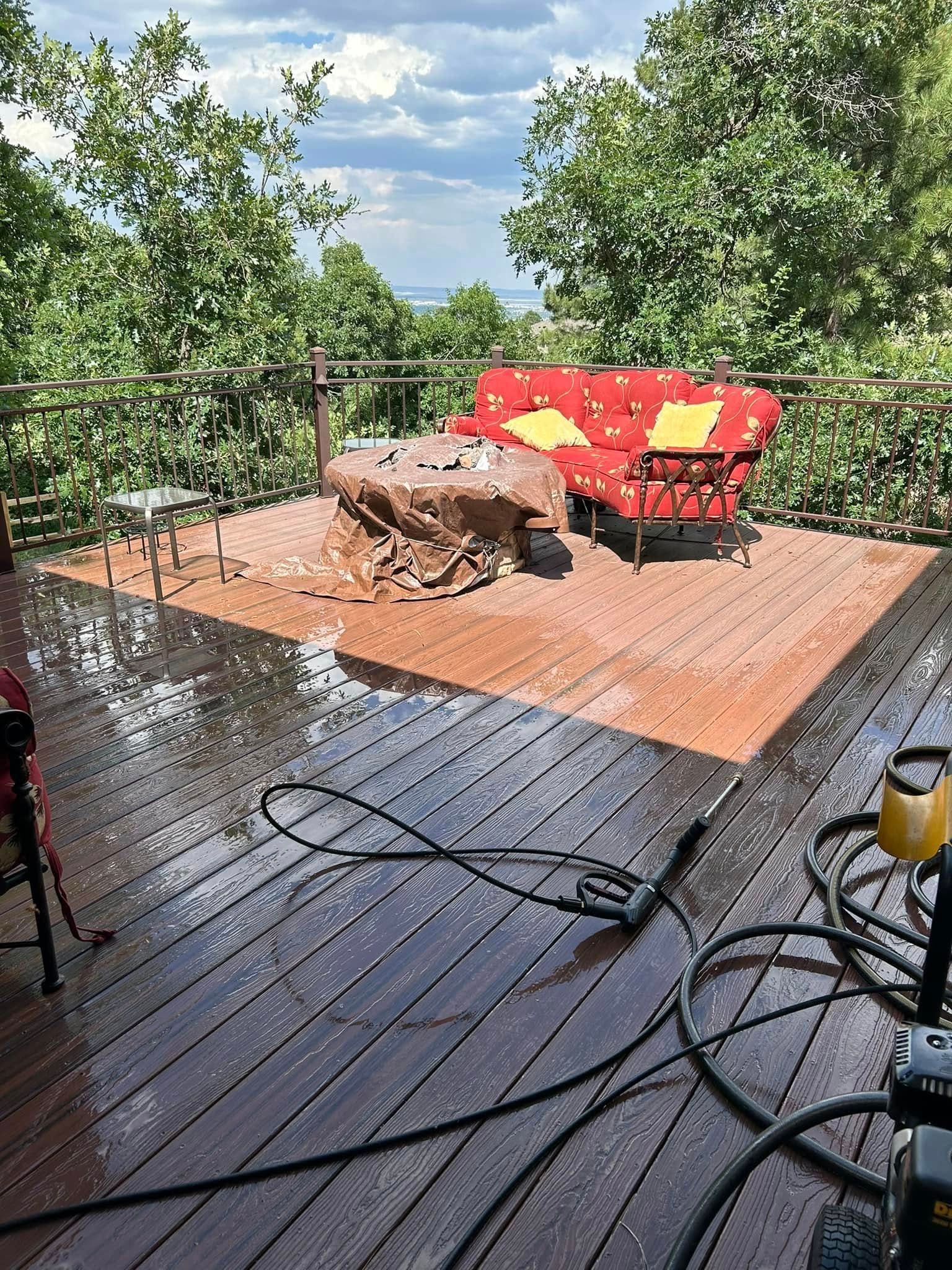 Wooden deck being cleaned with a pressure washer; a red couch and trees are in the background.
