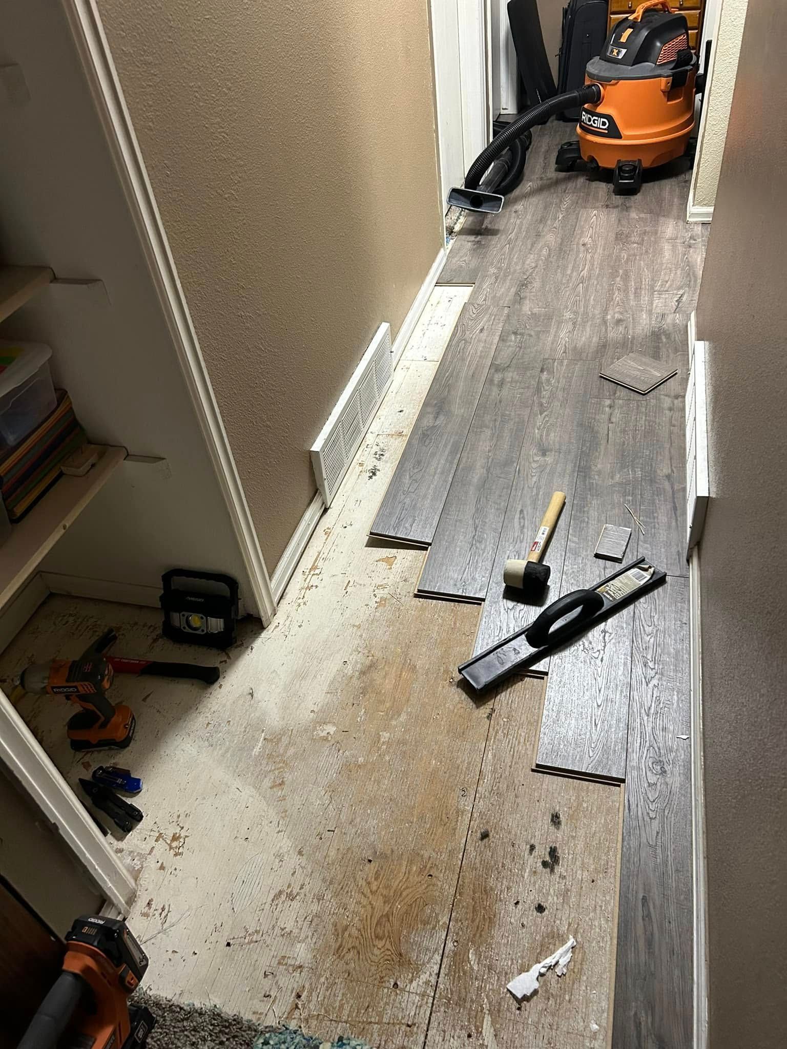 Hallway with laminate flooring being installed; tools and vacuum present.