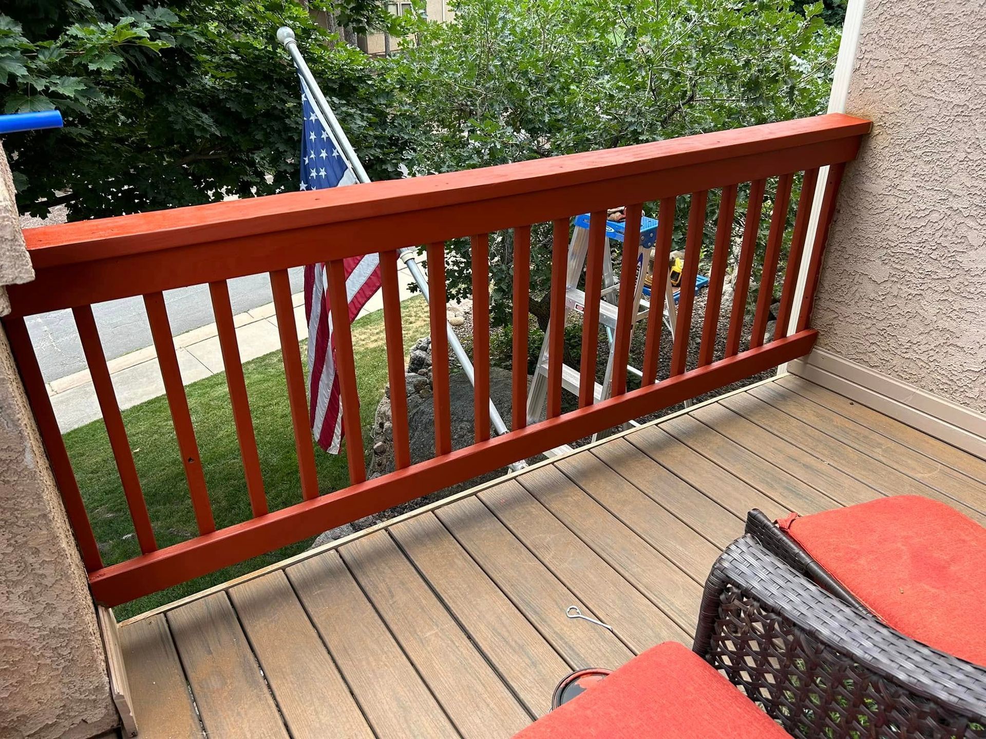 Balcony with reddish-brown railing and composite decking, partially visible American flag.