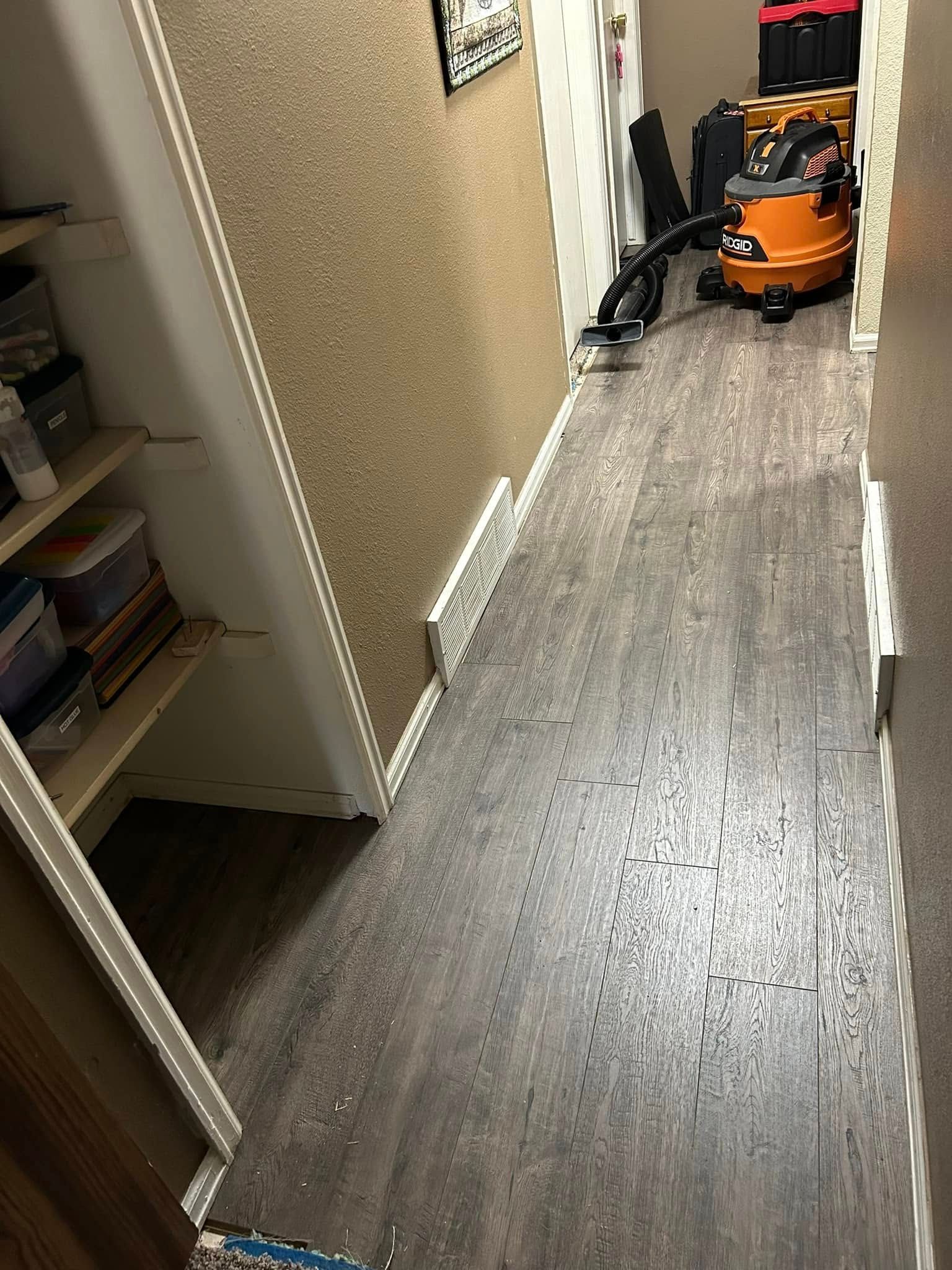 Narrow hallway with dark flooring, cork-covered wall, and a vacuum cleaner in the background.