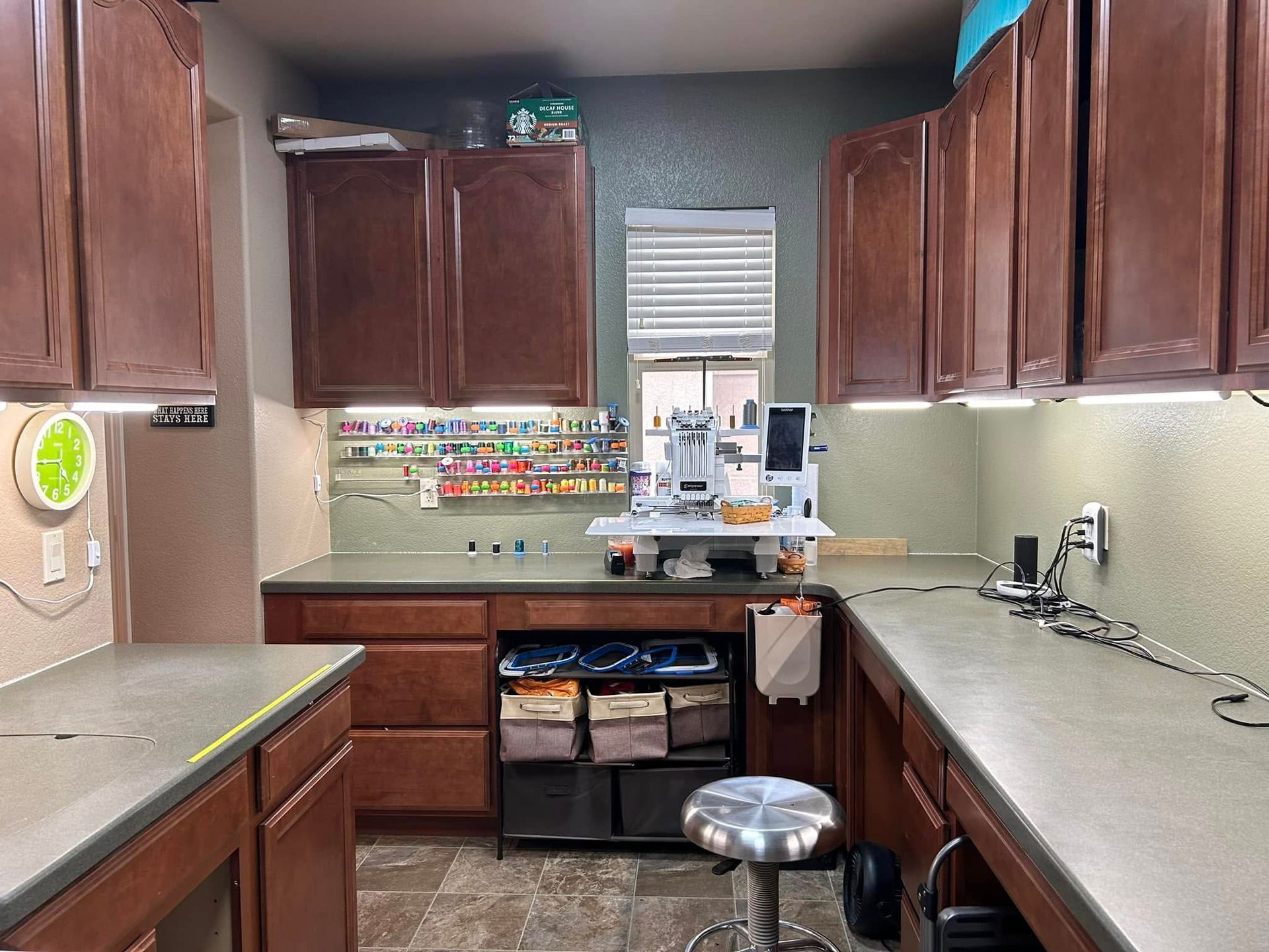 A craft room with dark brown cabinets, gray countertops, a sewing machine, and a stool.