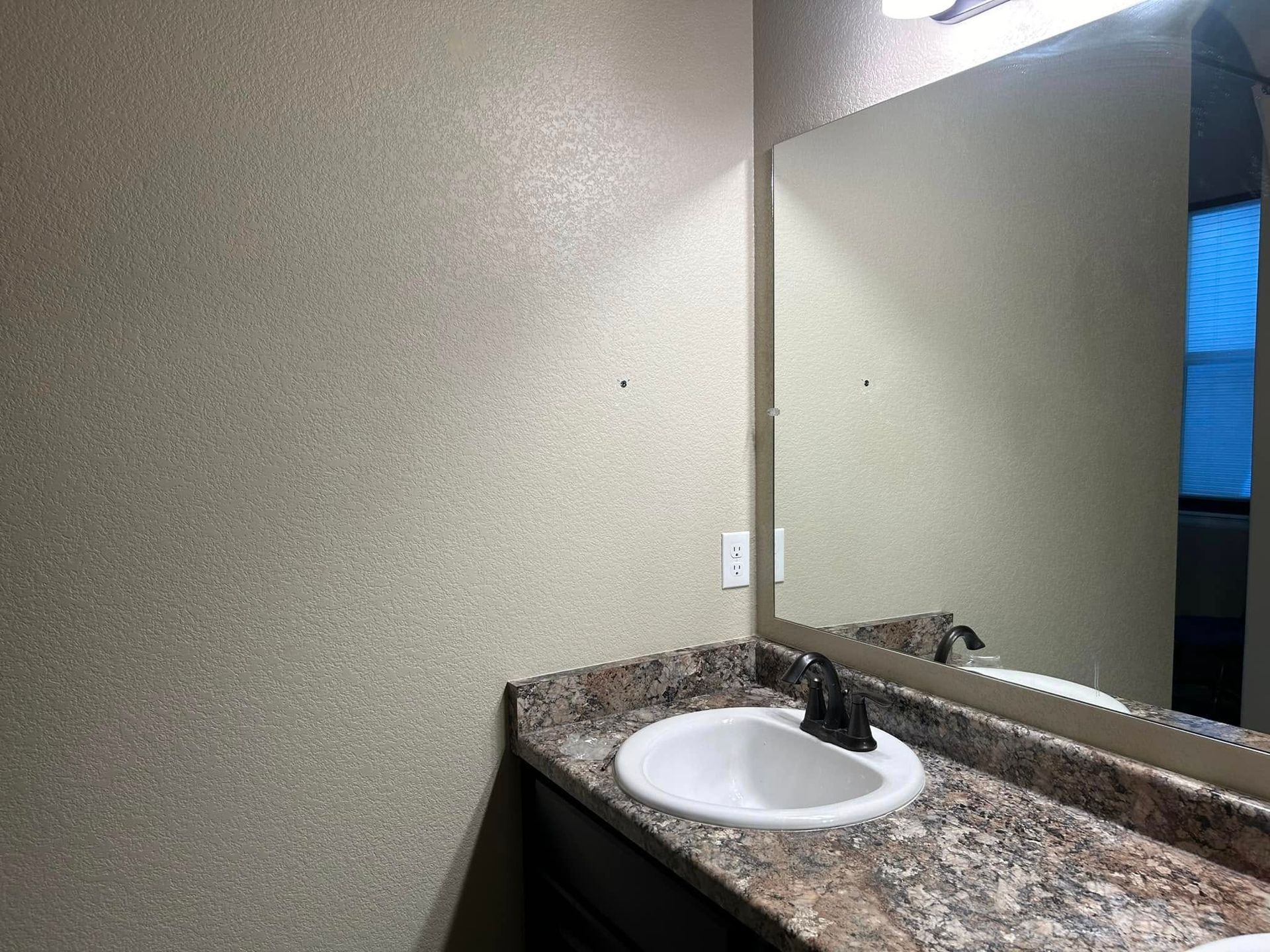 Bathroom with speckled beige walls, countertop sink, dark faucet, mirror reflecting a window.