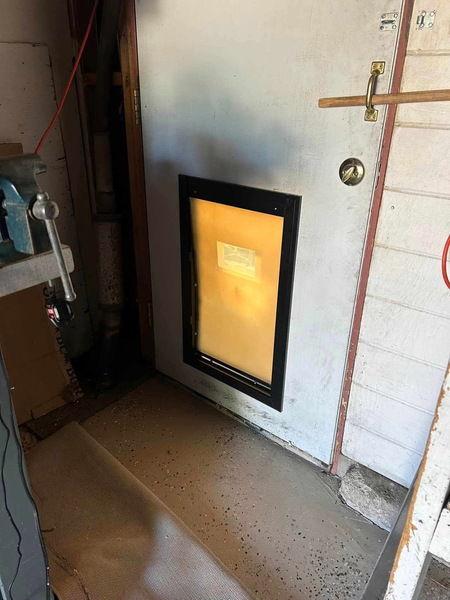 Door with a pet door, wood floors, and a cluttered workshop setting.