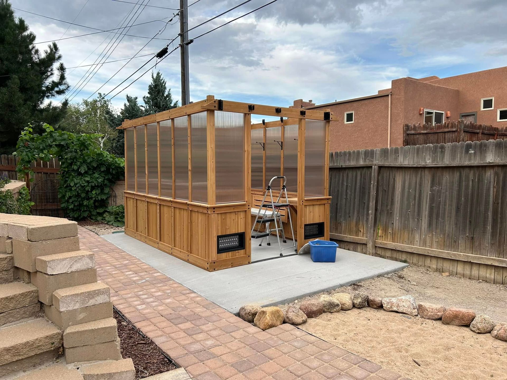 Outdoor shower stall with wooden frame and corrugated plastic walls; concrete patio.
