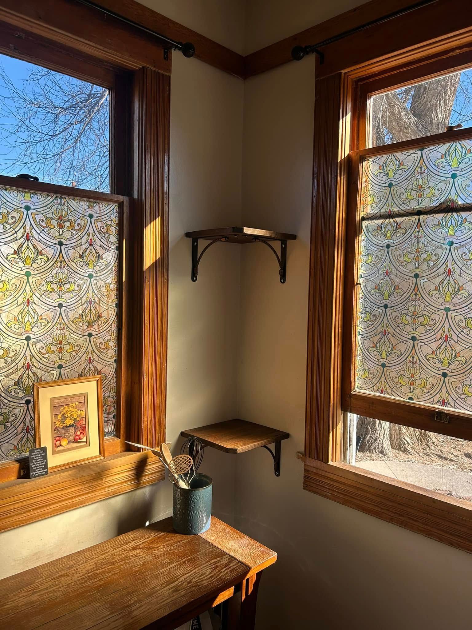 Corner nook with two windows and wooden shelves, lit by sunlight.