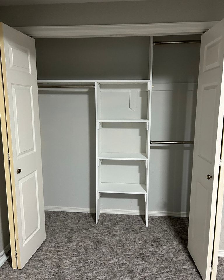 Empty closet with white doors and shelves. Gray walls and carpet.