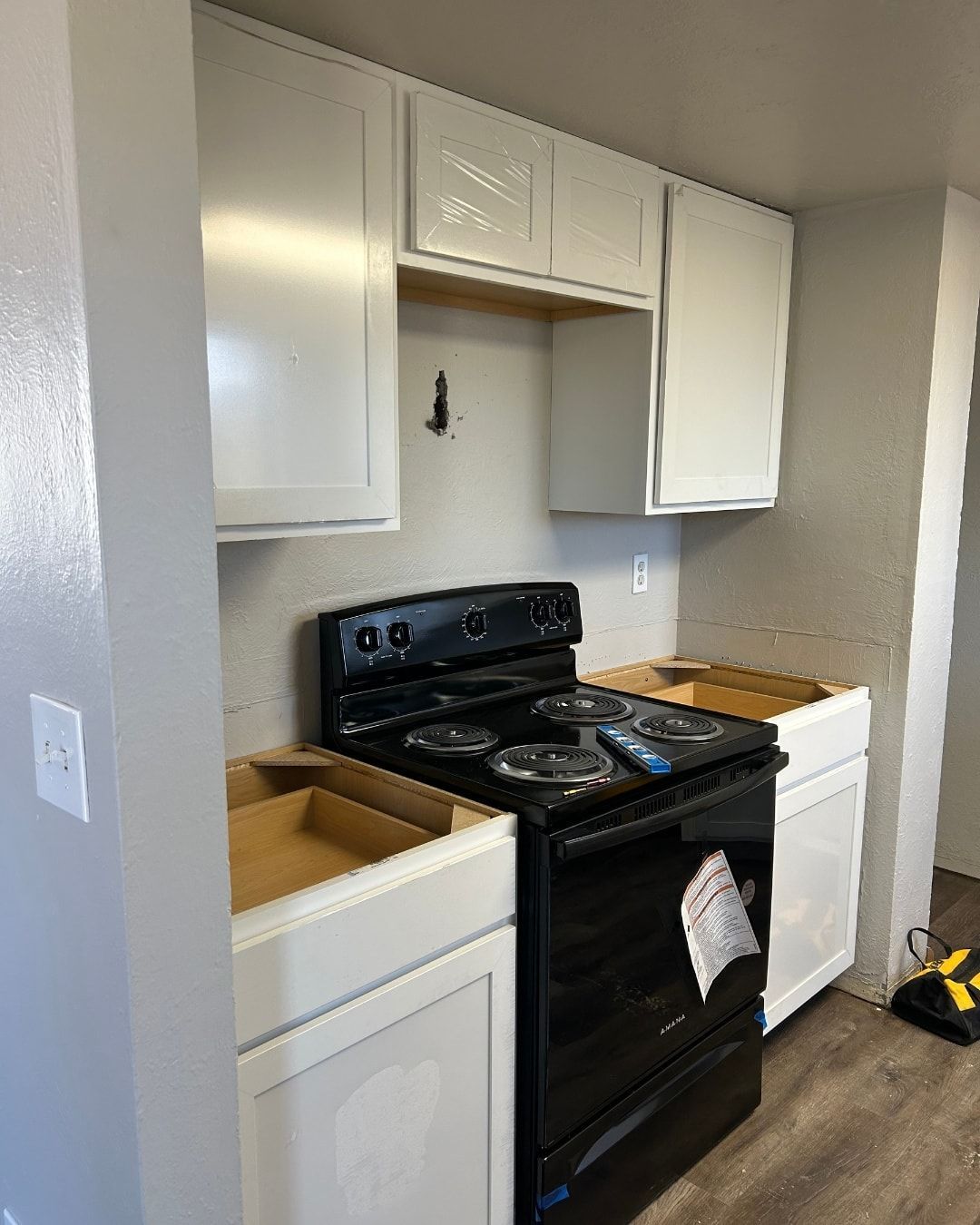 Kitchen under renovation: white cabinets, black stove, light grey walls, unfinished lower cabinets.