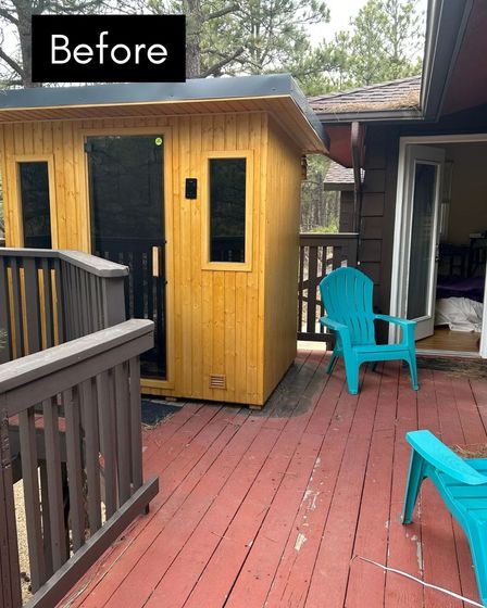 Outdoor sauna on a red deck, next to a house with a sliding glass door. Blue chairs are on the deck.