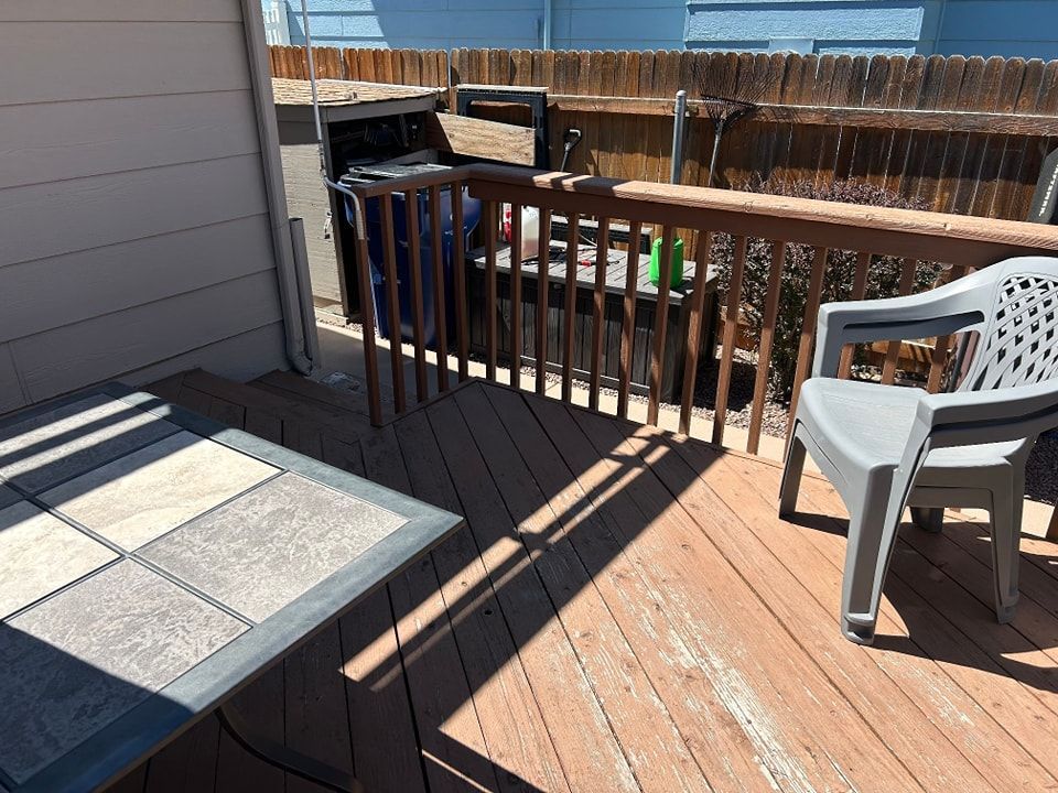 Wooden deck with table, chair, and grill; backyard setting.