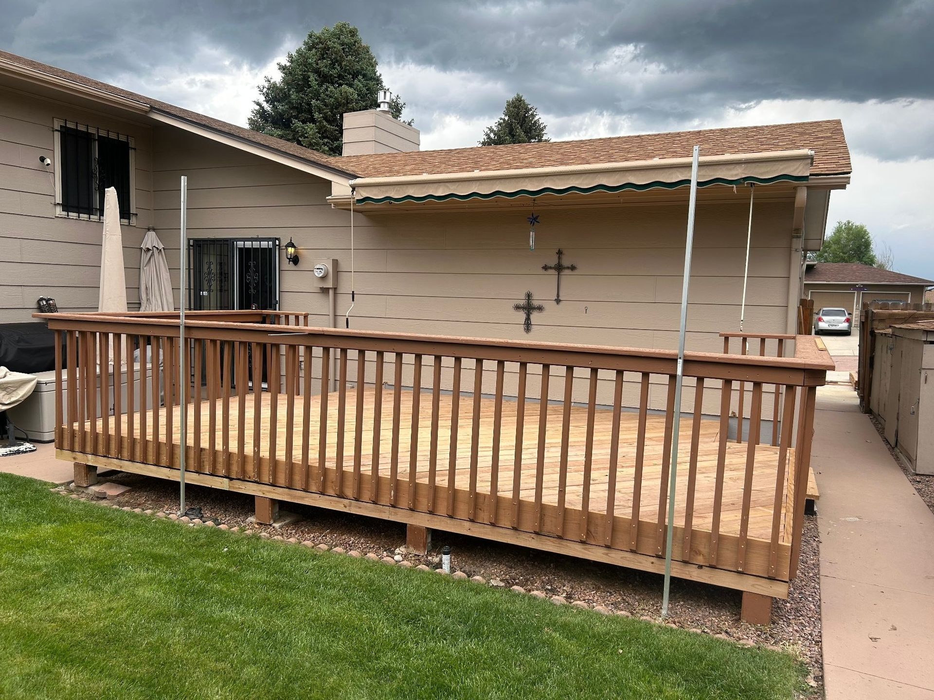 Wooden deck attached to a tan house with a grassy lawn and cloudy sky.