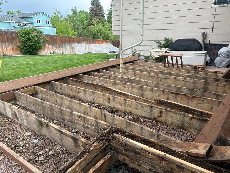 Partially dismantled wooden deck in a backyard; weathered wood, gravel ground.