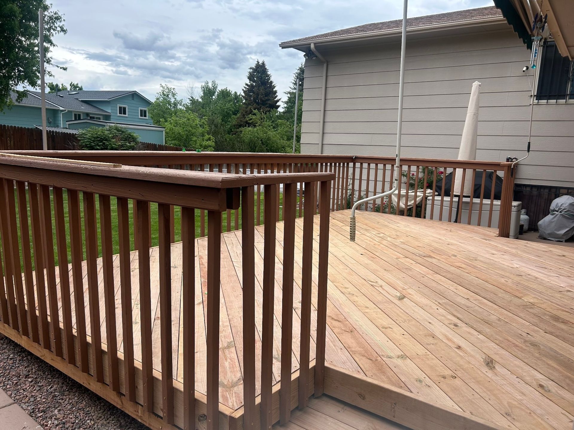 Wooden deck with railing, ramp, and a light-colored house in the background. Cloudy sky overhead.
